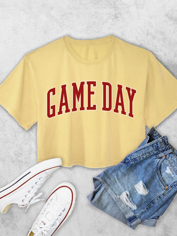 Yellow t-shirt with 'GAME DAY' text, paired with denim shorts and white sneakers on a light gray background