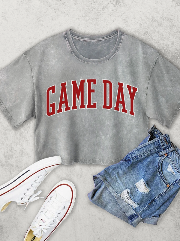 Gray t-shirt with 'GAME DAY' text, white sneakers, and denim shorts on a light gray background