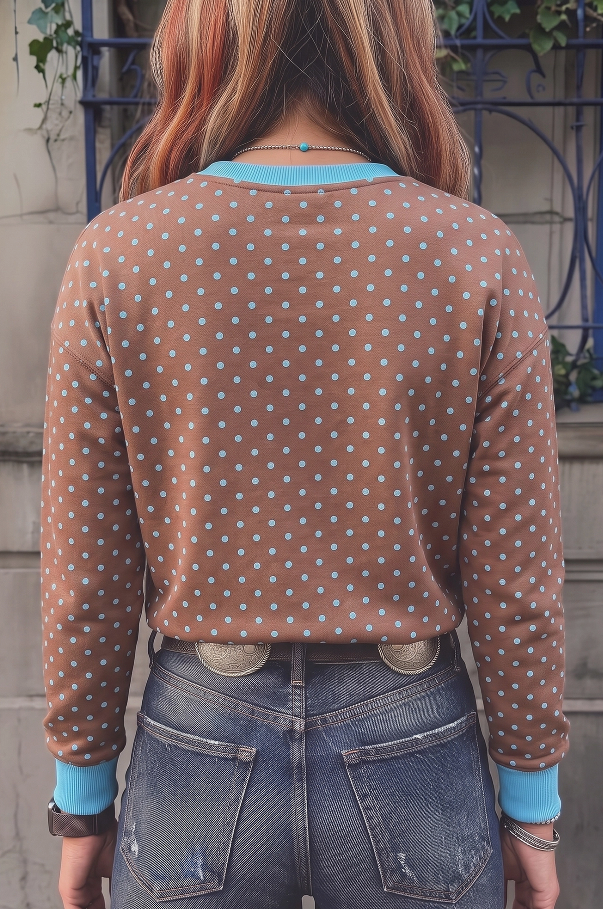 A person viewed from behind wearing a brown long-sleeve top with a light blue and white polka dot pattern, light blue ribbed collar and cuffs, paired with blue jeans.